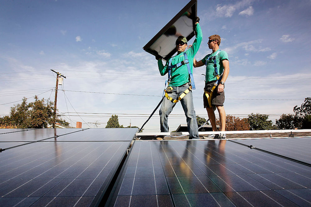 عاملان يركبان ألواحًا شمسية على سطح أحد المباني