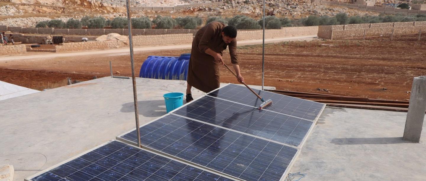 لاجئ سوري ينظف ألواحًا شمسية على سطح منزله