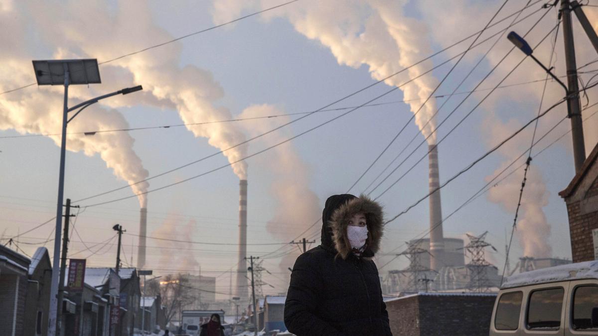 رجل أمام أبراج محطة كهرباء تعمل بالفحم في الصين